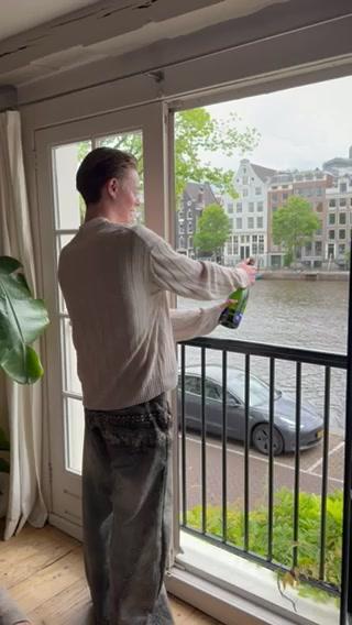 A man sprays a plant while looking out the window at a canal